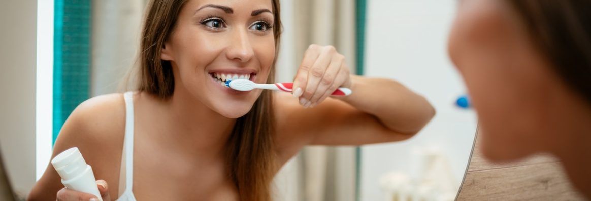 Beautiful young woman brushing teeth in front of her bathroom mirror. Selective focus.